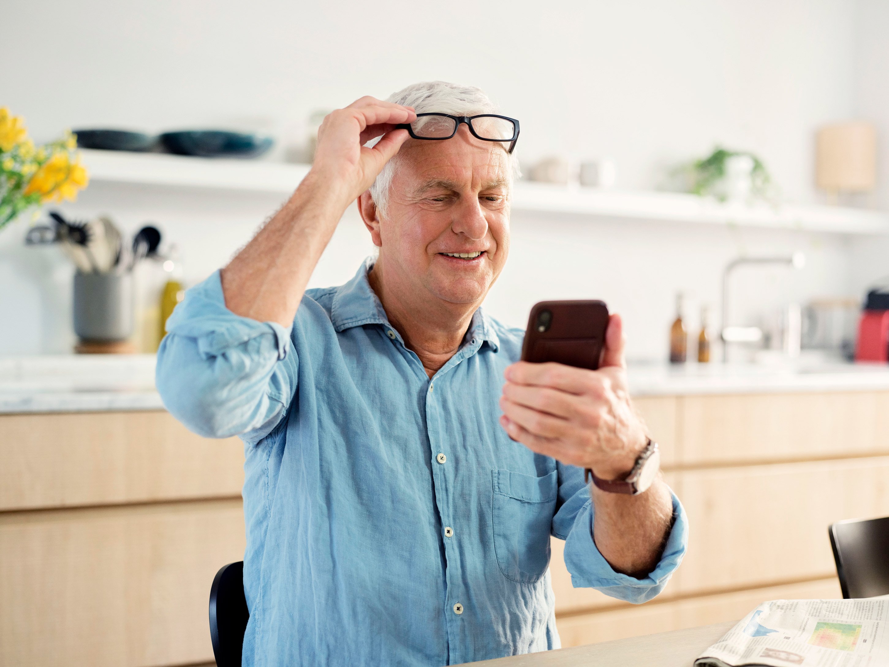 An elderly gentleman holding a phone in his right hand and looking at it and adjusting his glasses with his left hand