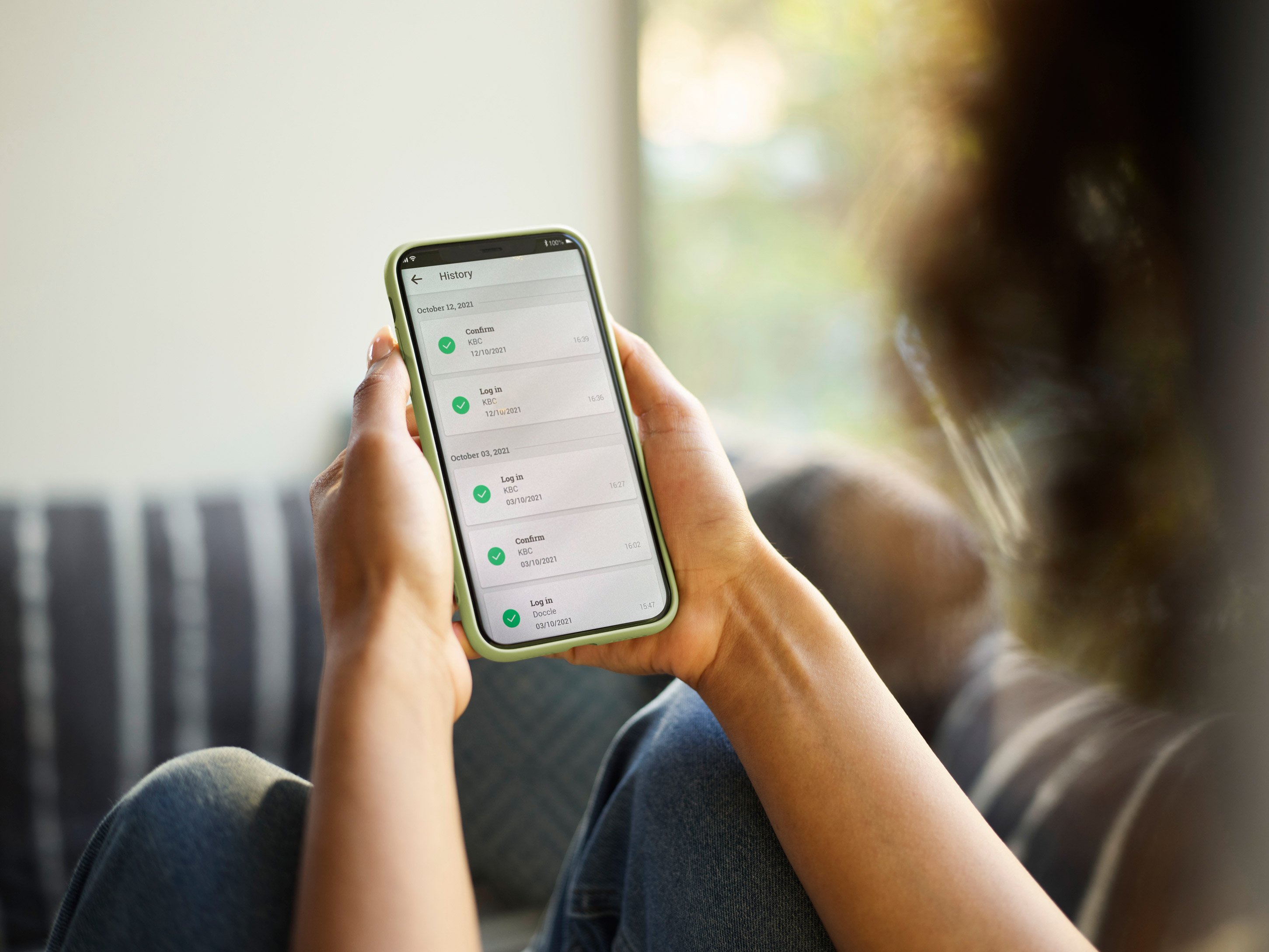 A woman sitting on a couch and holding her phone with both hands, she is looking at the phone