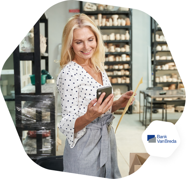 A woman with long blonde hair and a dotted top is standing and looking at her phone